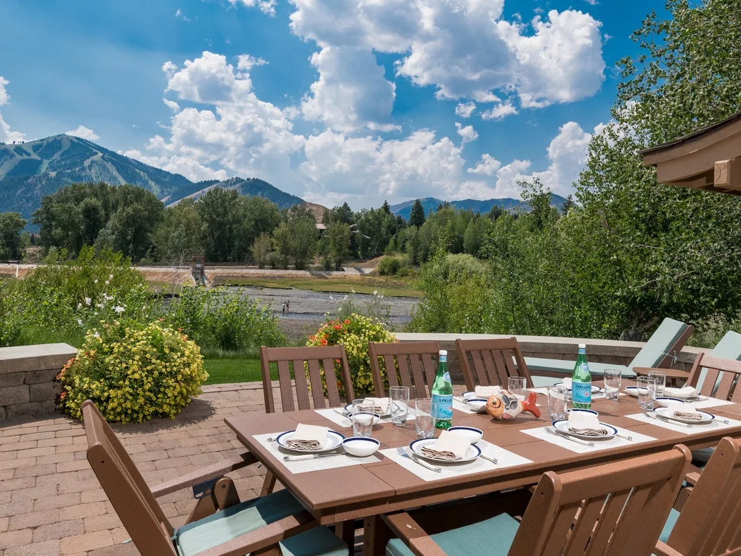 Una zona de comedor al aire libre ofrece vistas a un valle verde y montañas.
