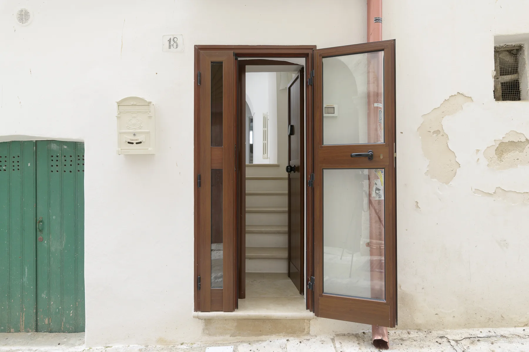 Una entrada abierta deja ver una escalera tras una pared exterior clara.