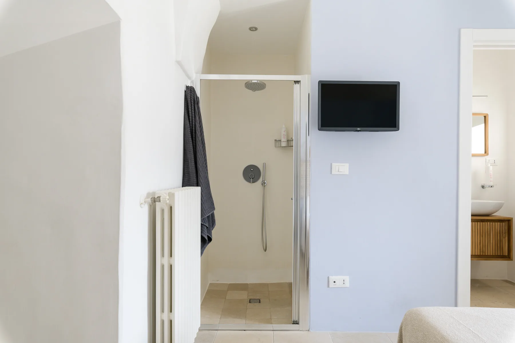 Un baño con una ducha de vidrio y un televisor montado en la pared.
