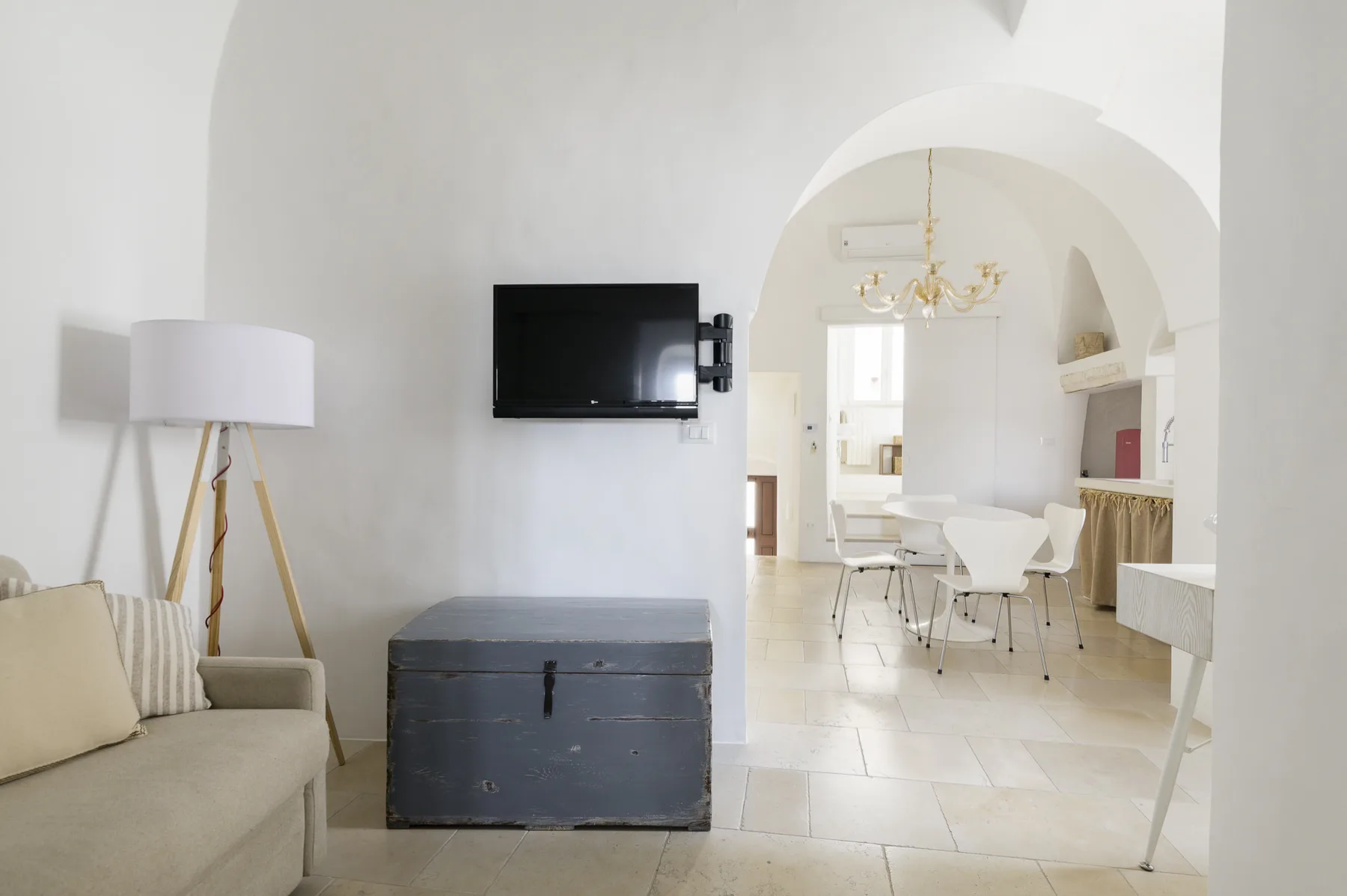 A bright living area with a sofa, television, and an arched opening to a dining space.