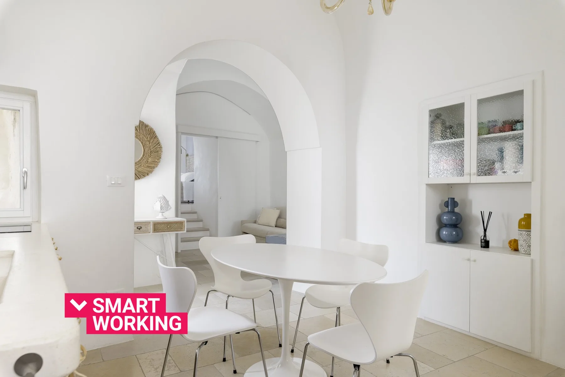 Un comedor luminoso con una mesa blanca y asientos bajo un arco.