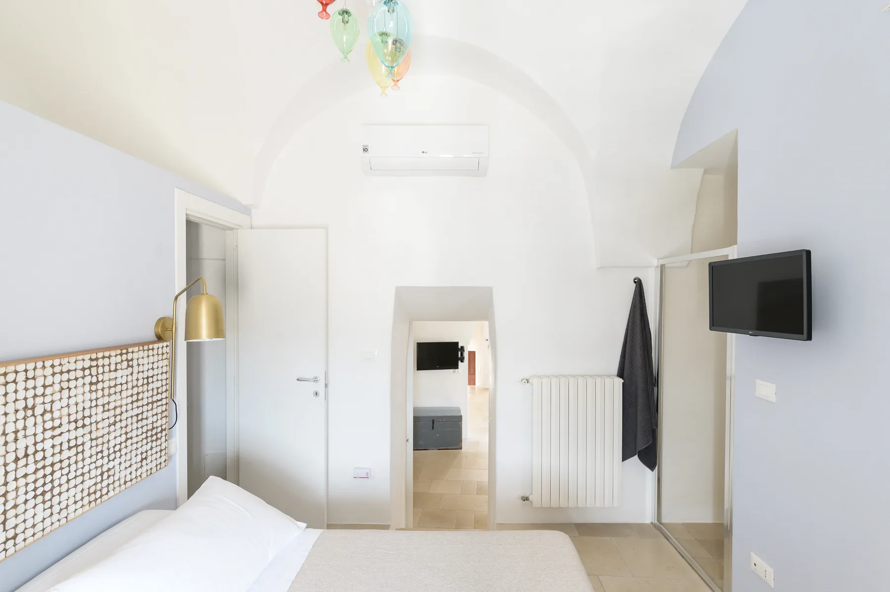 Un dormitorio luminoso con una cama, un televisor en la pared y un radiador blanco.