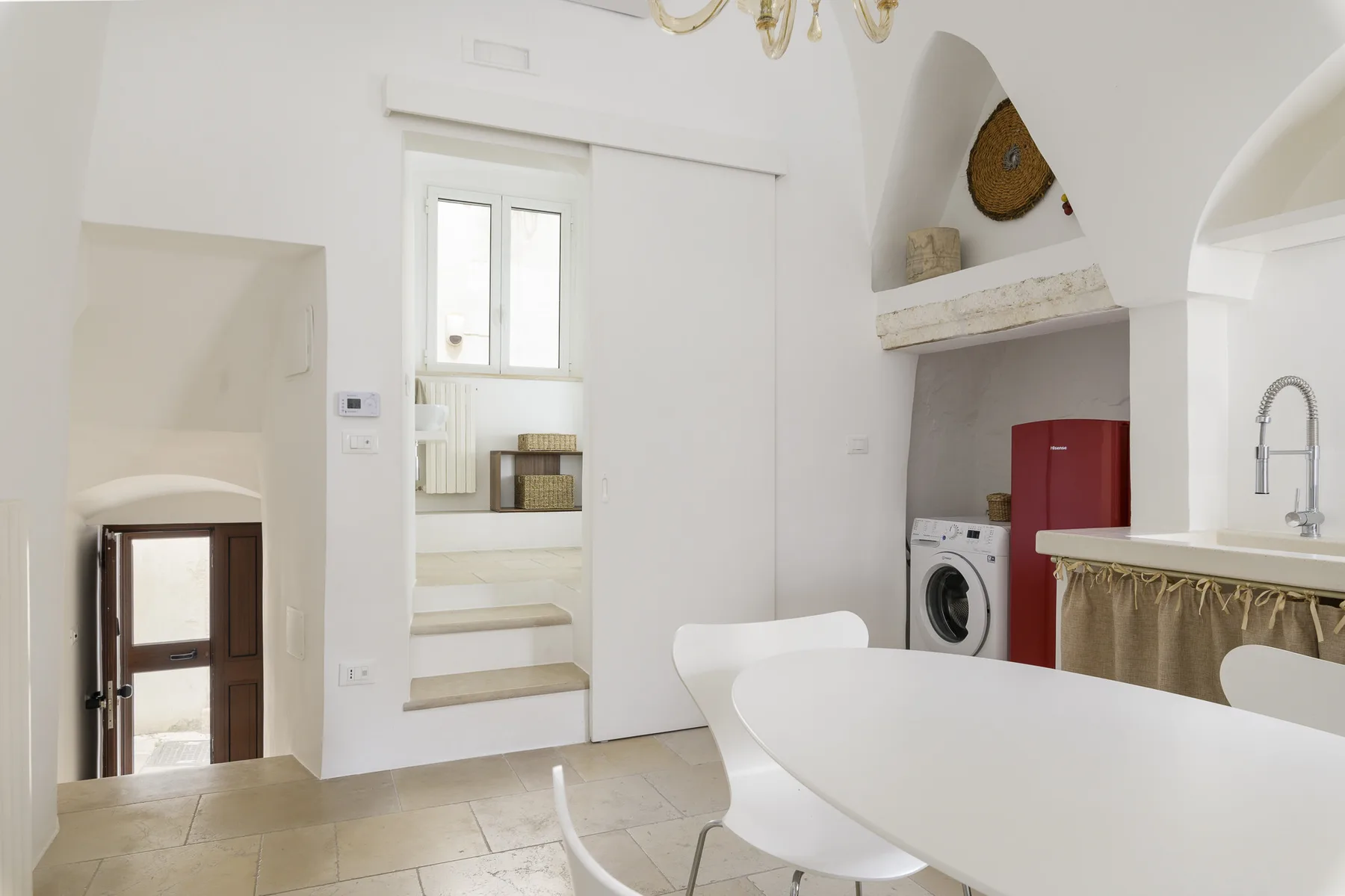 Un comedor luminoso con una mesa blanca y sillas junto a una cocina compacta.