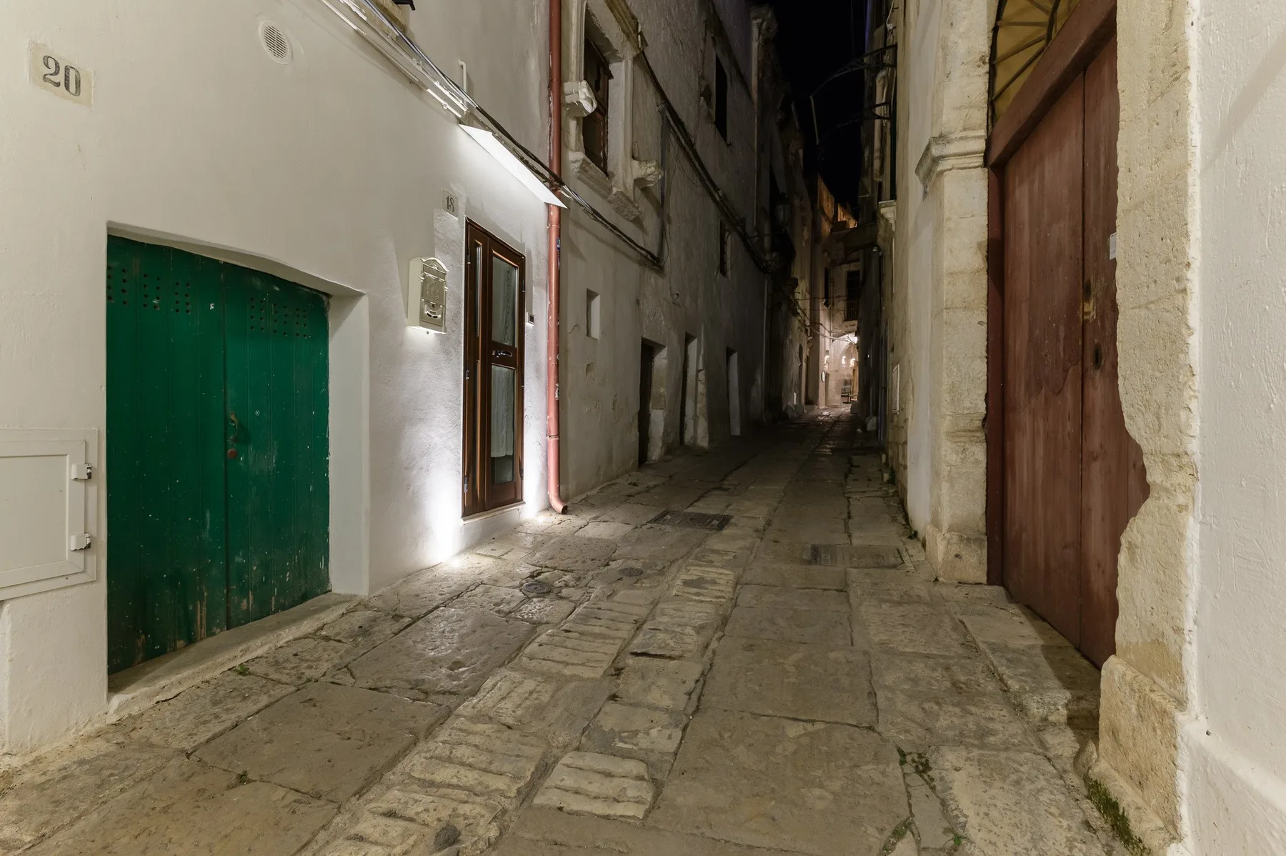 Un callejón estrecho pavimentado de piedra transcurre entre edificios antiguos por la noche.