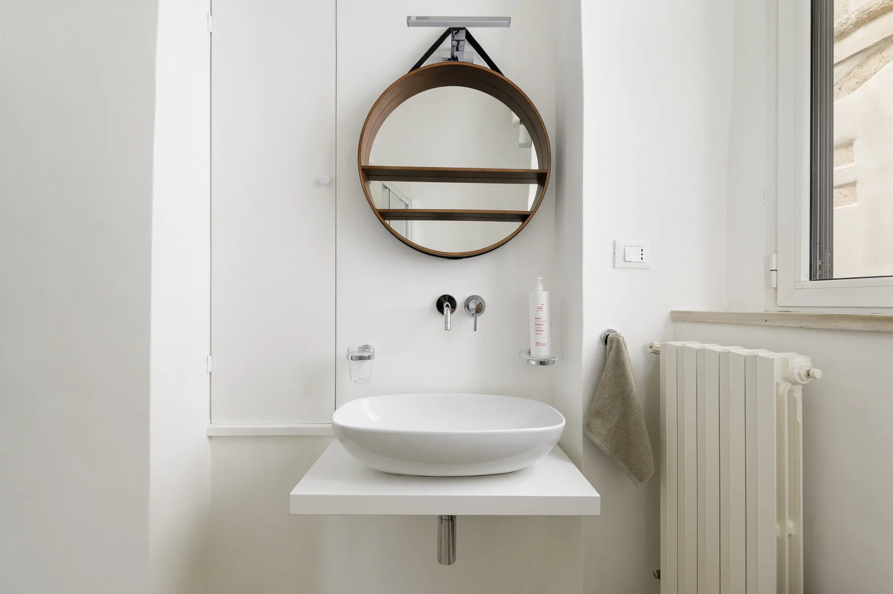 Un lavabo de baño luminoso con espejo redondo, lavabo de recipiente y radiador.