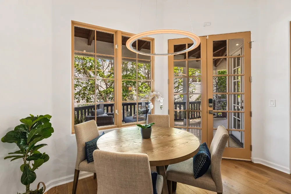 Un comedor luminoso con una mesa redonda de madera junto a altas puertas de vidrio.