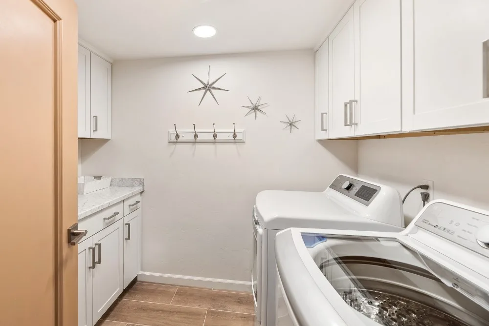 Un cuarto de lavandería con lavadoras, armarios blancos y un perchero de pared.