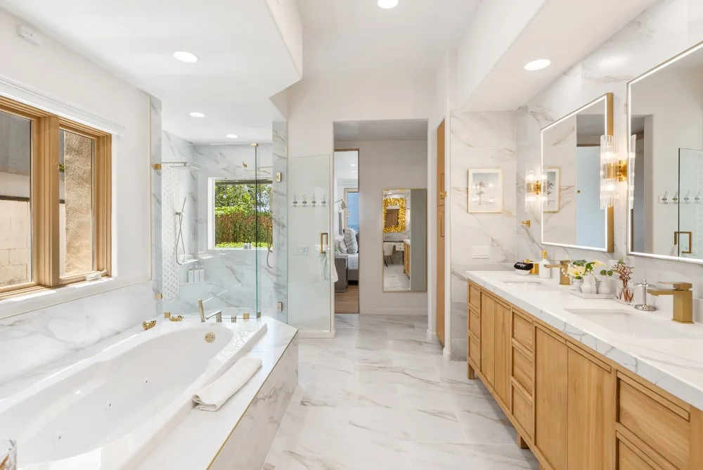 Un baño luminoso con bañera, tocador doble y superficies con vetas de mármol.