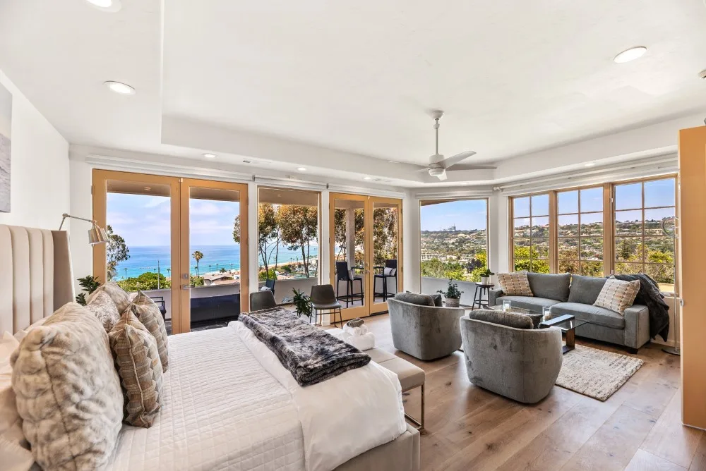 Un dormitorio luminoso con zona de estar y amplias ventanas con vistas a la costa.