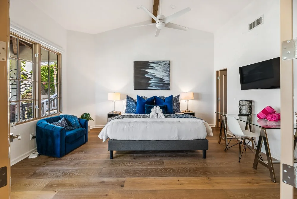Un dormitorio luminoso con una cama vestida de blanco y almohadas azules.