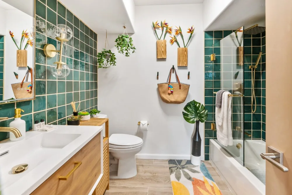 Un baño luminoso con paredes de azulejos verdes, un tocador y una ducha de cristal.