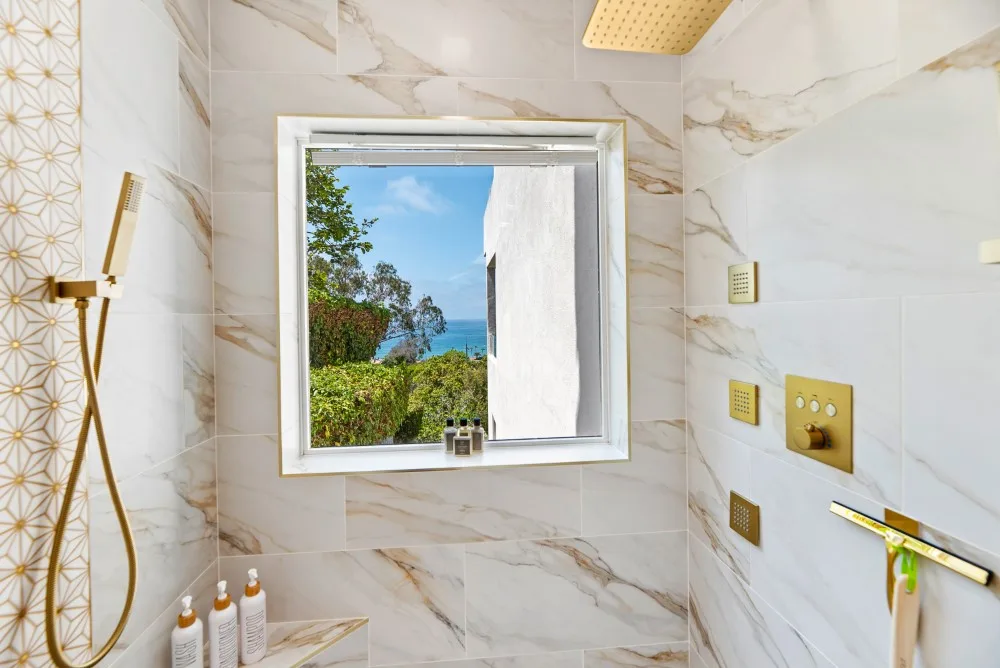 Un baño alicatado con ducha y una ventana con vistas a vegetación y agua.