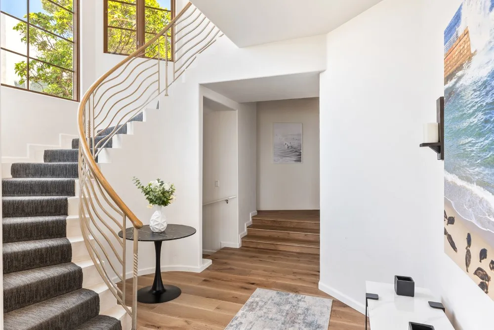 Una entrada luminosa con una escalera curva, suelo de madera y una mesita auxiliar.