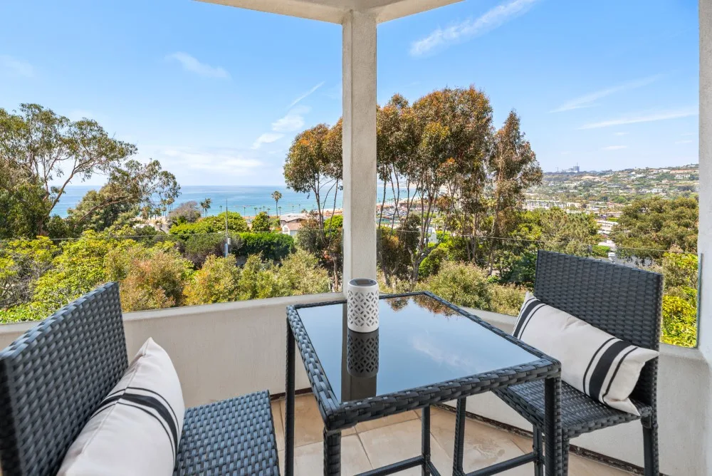 Un patio cubierto con asientos al aire libre ofrece vistas de árboles, la costa y edificios lejanos.