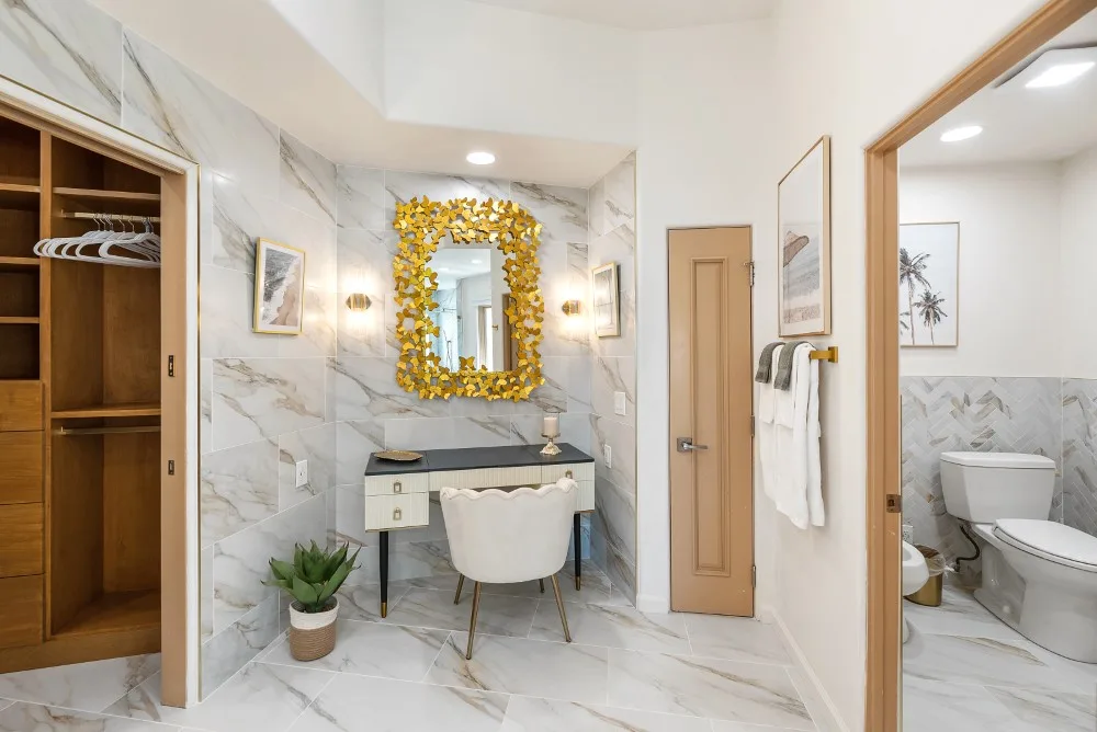 Un baño luminoso con tocador, espejo y una puerta abierta hacia un inodoro.