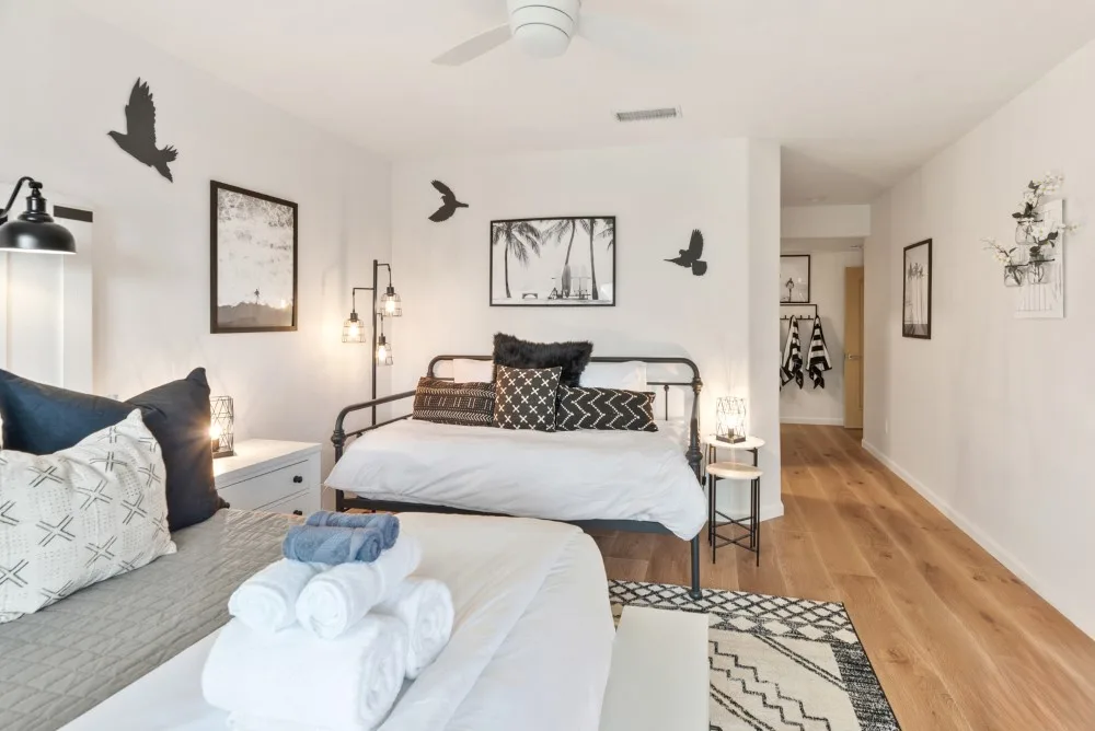 Un dormitorio luminoso con dos camas, cuadros enmarcados y suelo de madera.