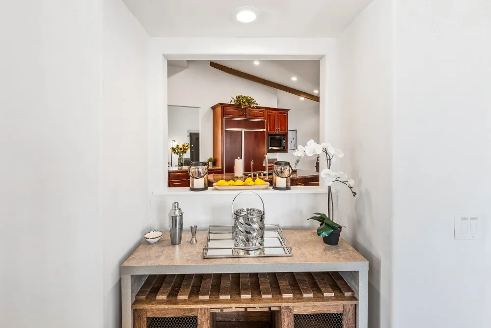 Un comedor luminoso con un aparador de madera adornado con cristalería y una planta con flores.