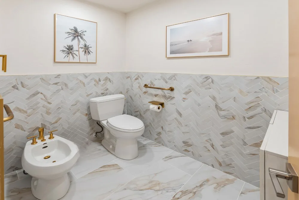 Un baño con inodoro, lavabo y azulejos claros con motivos.