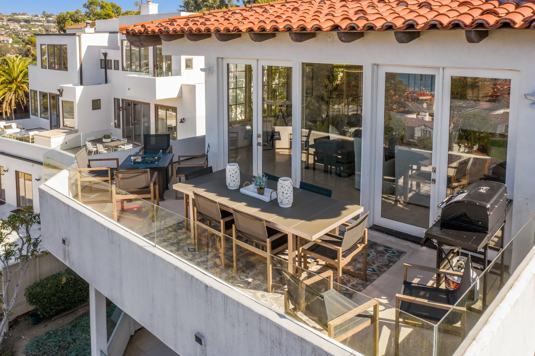 Una terraza exterior con una mesa larga, asientos y puertas de vidrio.