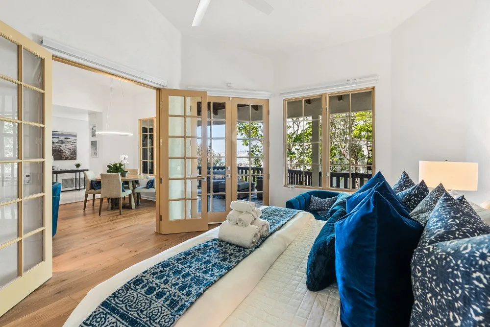 Una sala luminosa con cojines azules y puertas de vidrio abiertas a un balcón.
