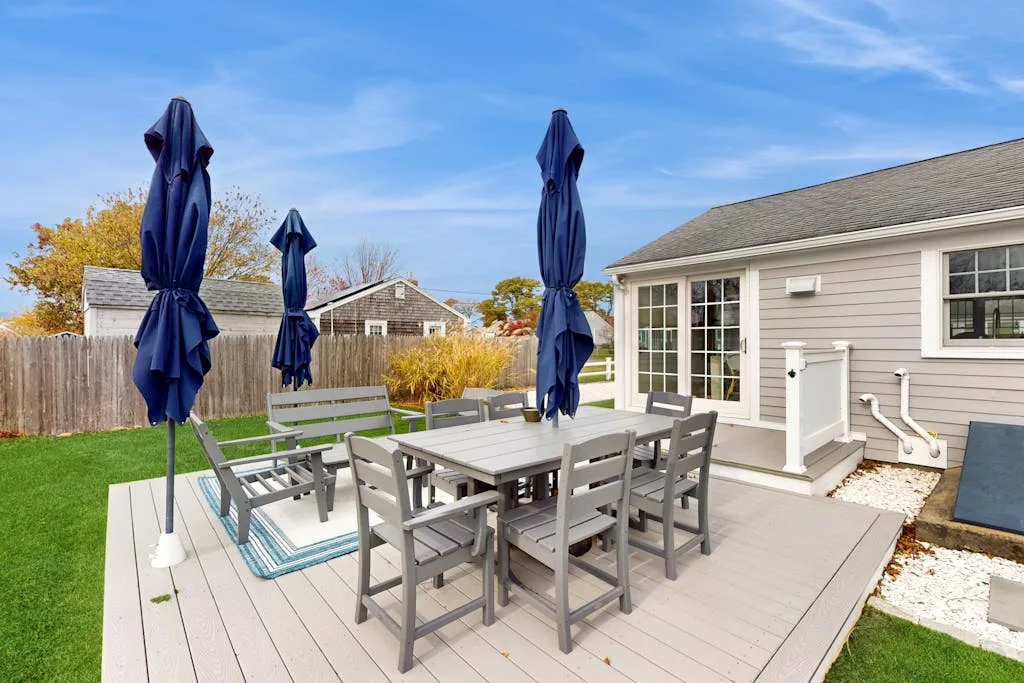 An outdoor dining area with patio seating and closed umbrellas beside a house.