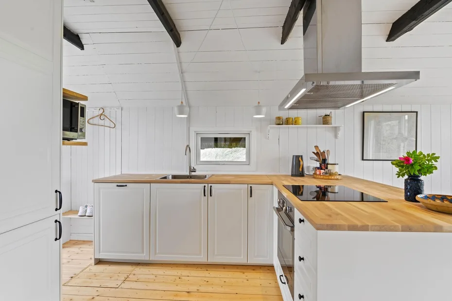 Una cocina luminosa con gabinetes blancos, encimeras de madera y una superficie de cocción central.
