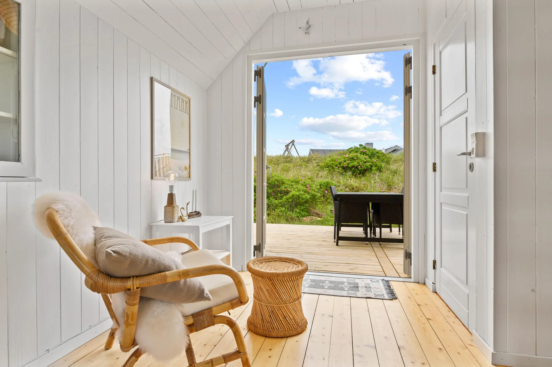 A bright sitting area opens through a doorway onto a wooden deck and green landscape.