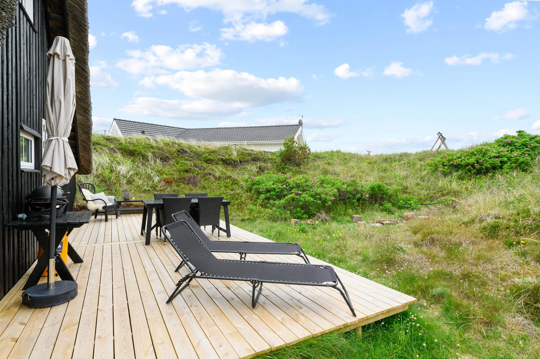 An outdoor deck with lounge seating overlooks a grassy, shrub-covered landscape.