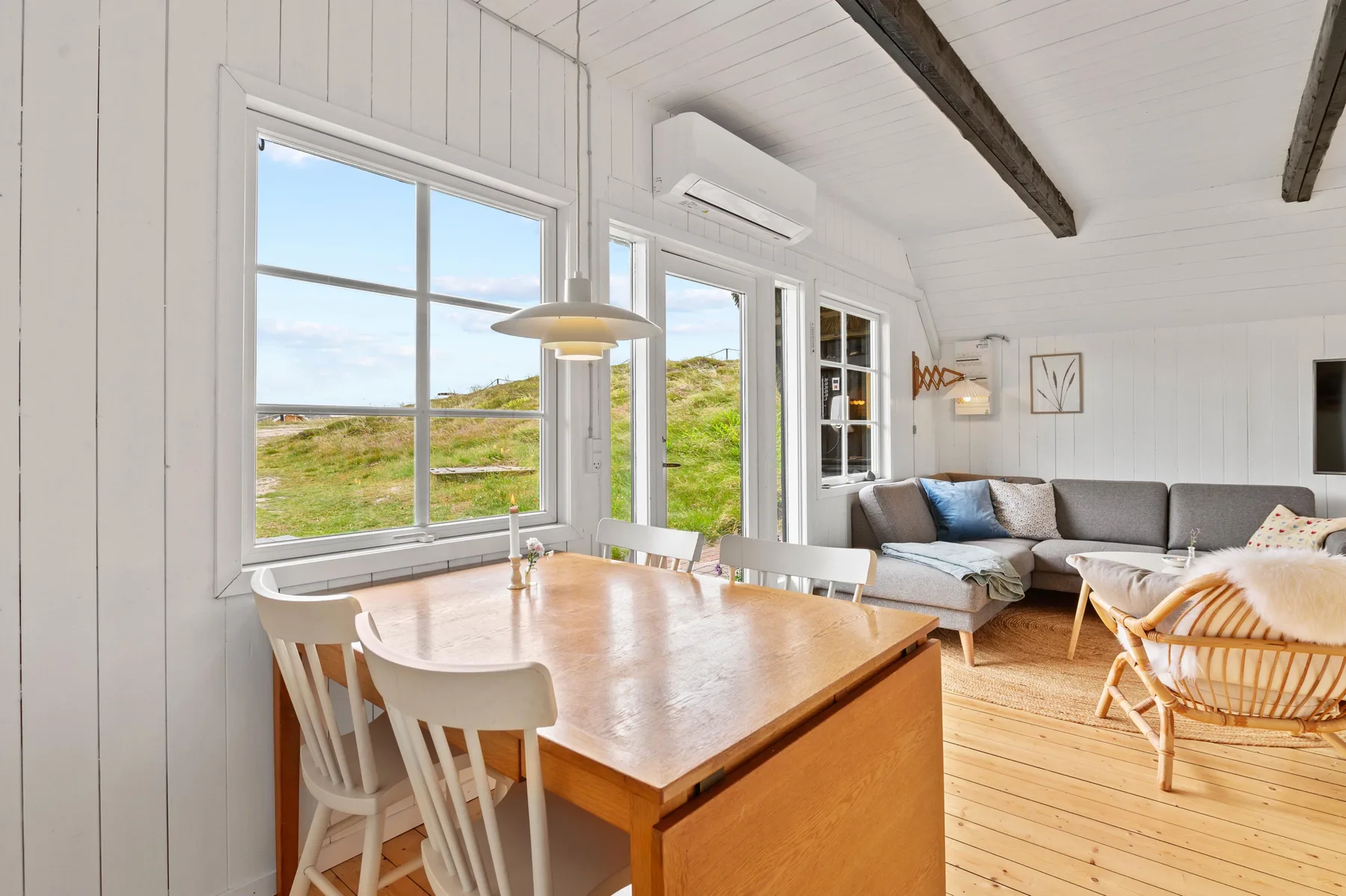 A bright dining and living area with a wooden table and seating beside large windows.