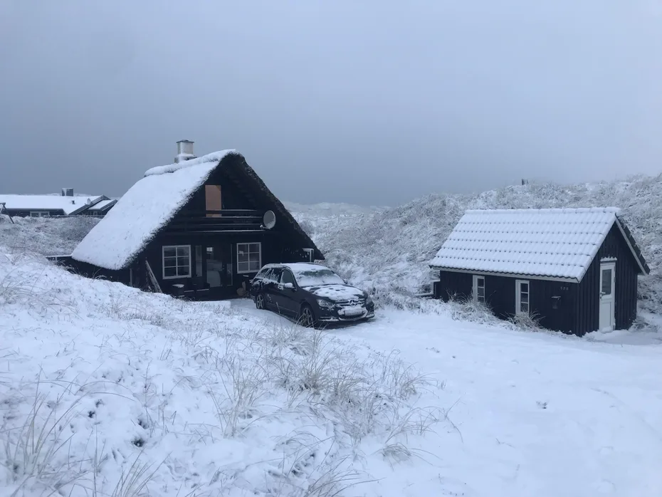 Snow-covered cabins stand beside a parked car in a snowy landscape.