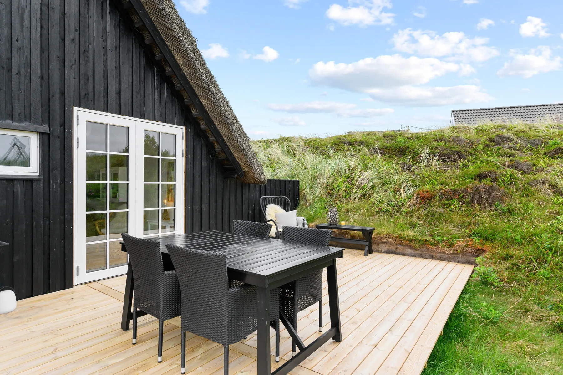 An outdoor dining area sits on a wooden deck beside a dark-sided building.