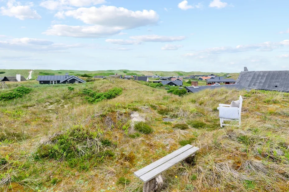 A grassy outdoor area with a bench and distant buildings beneath a cloudy sky.