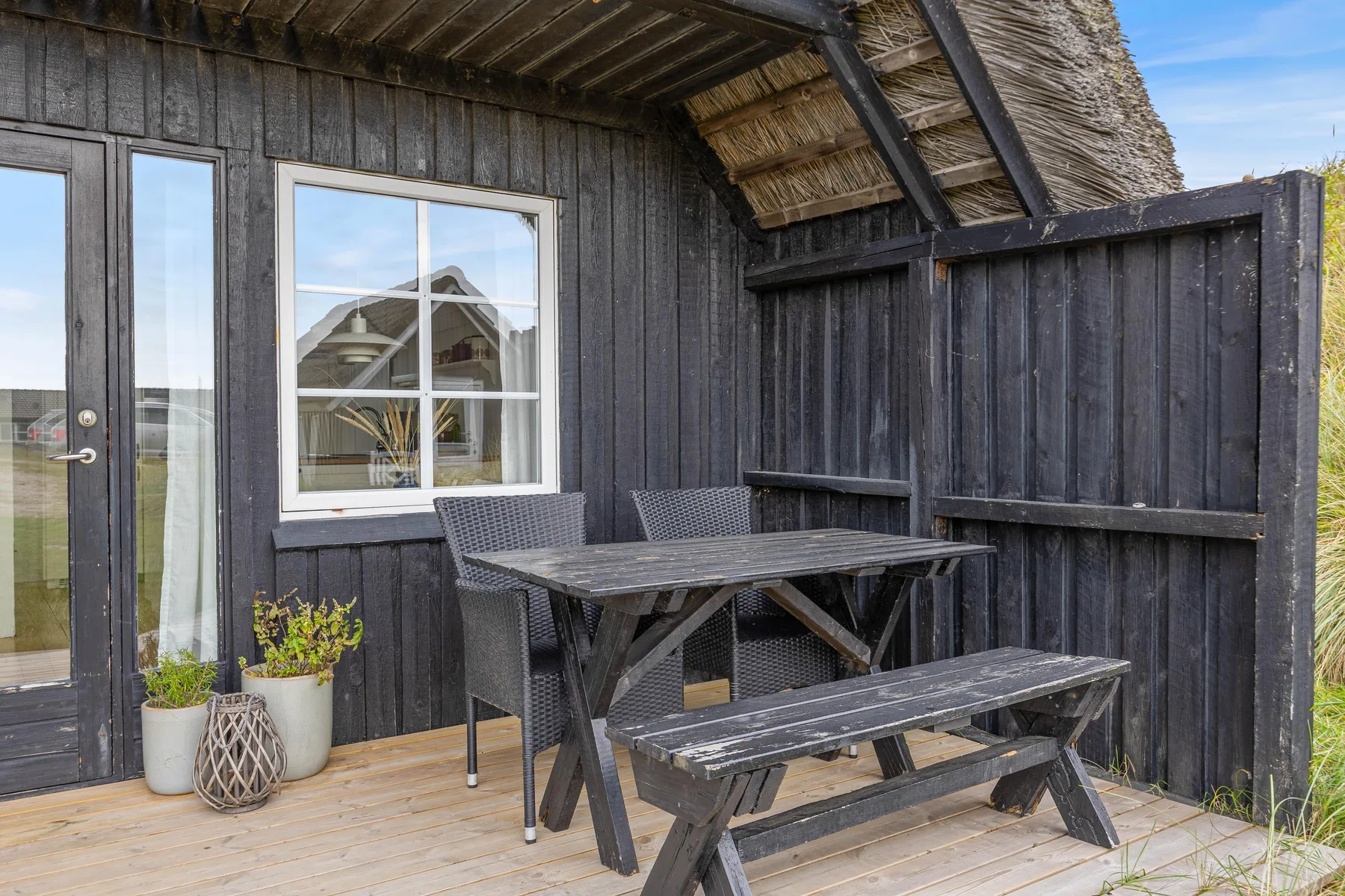 An outdoor dining area beside a dark wooden building, with a picnic table and chairs.