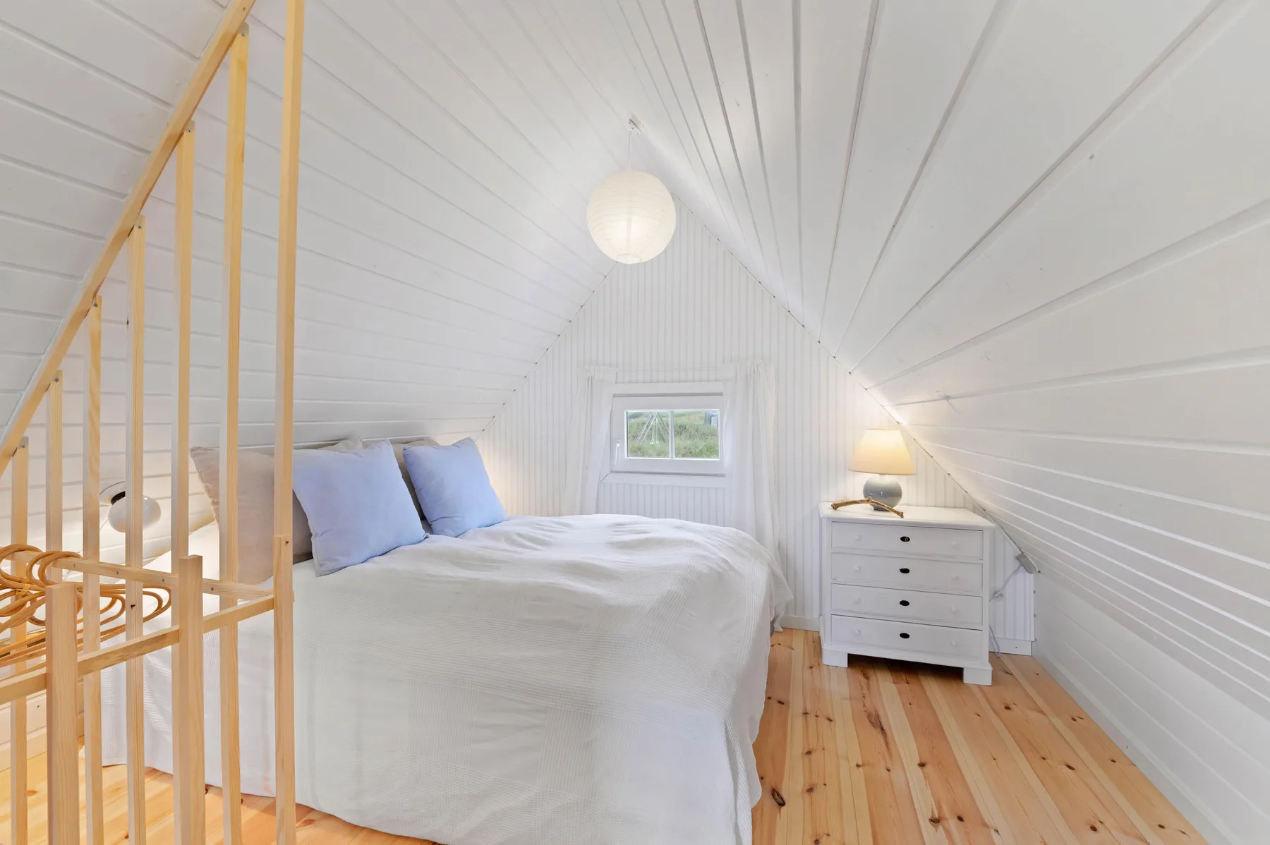 A bedroom with a bed, a small window, and a white dresser.
