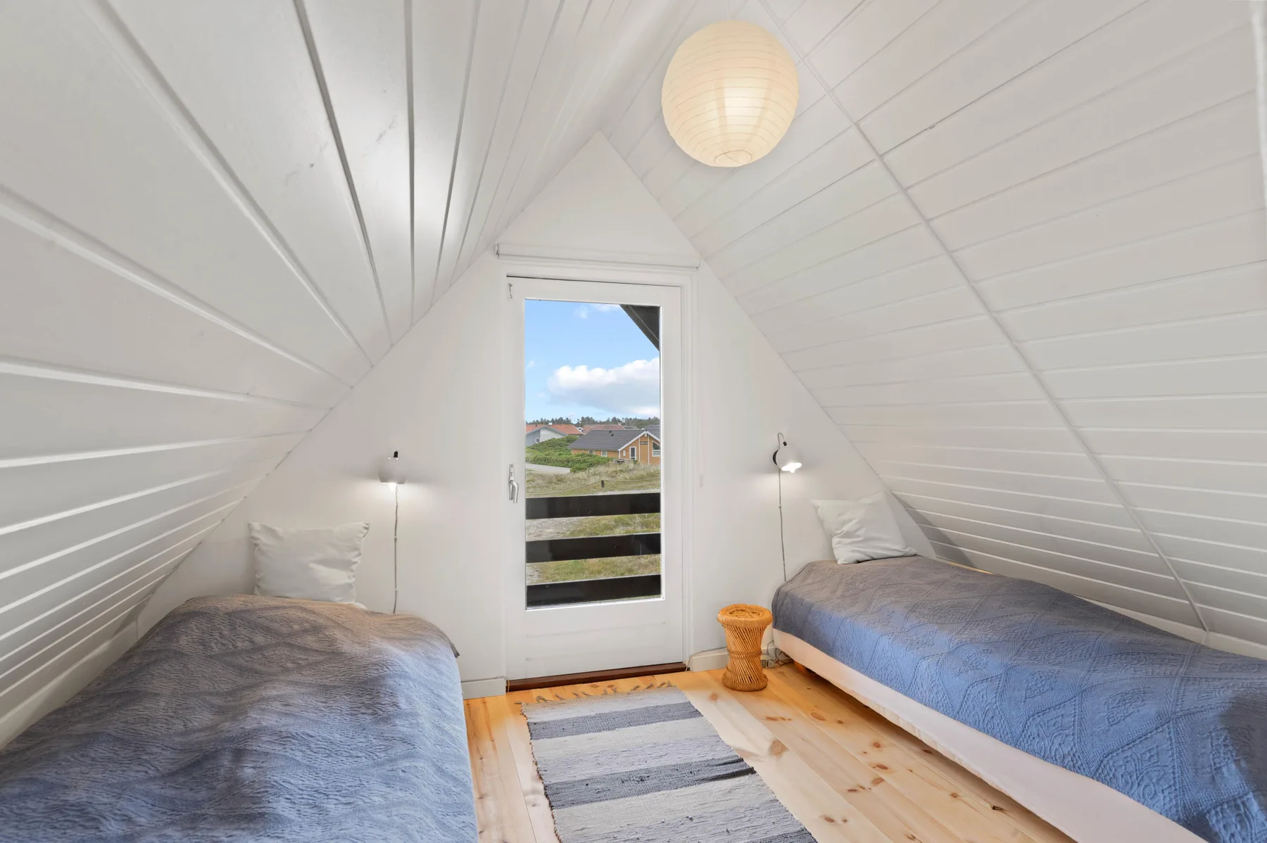 A bright attic bedroom with two beds and a door opening onto a balcony.