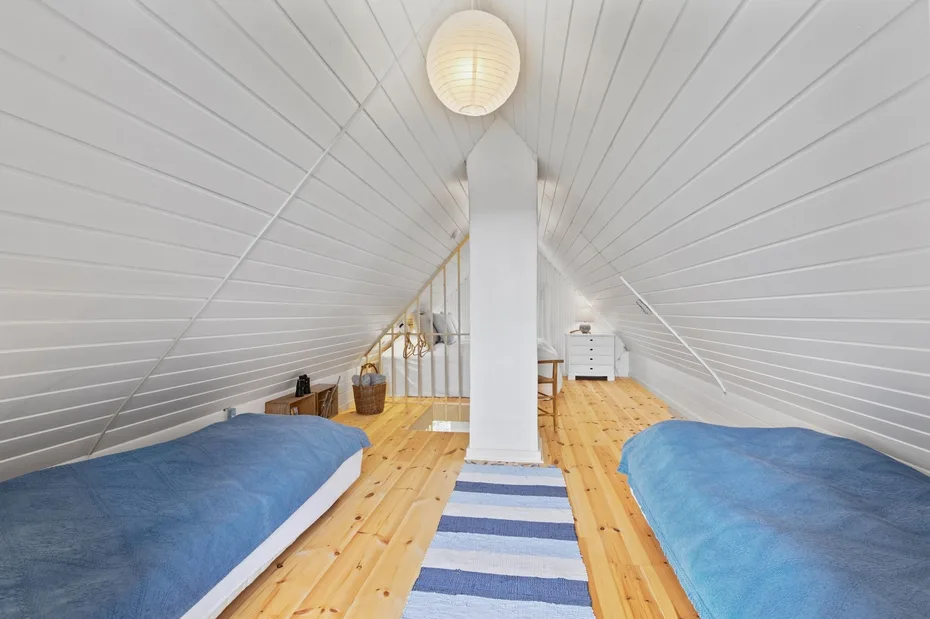 An attic bedroom with two beds, a central support column, and a striped rug.