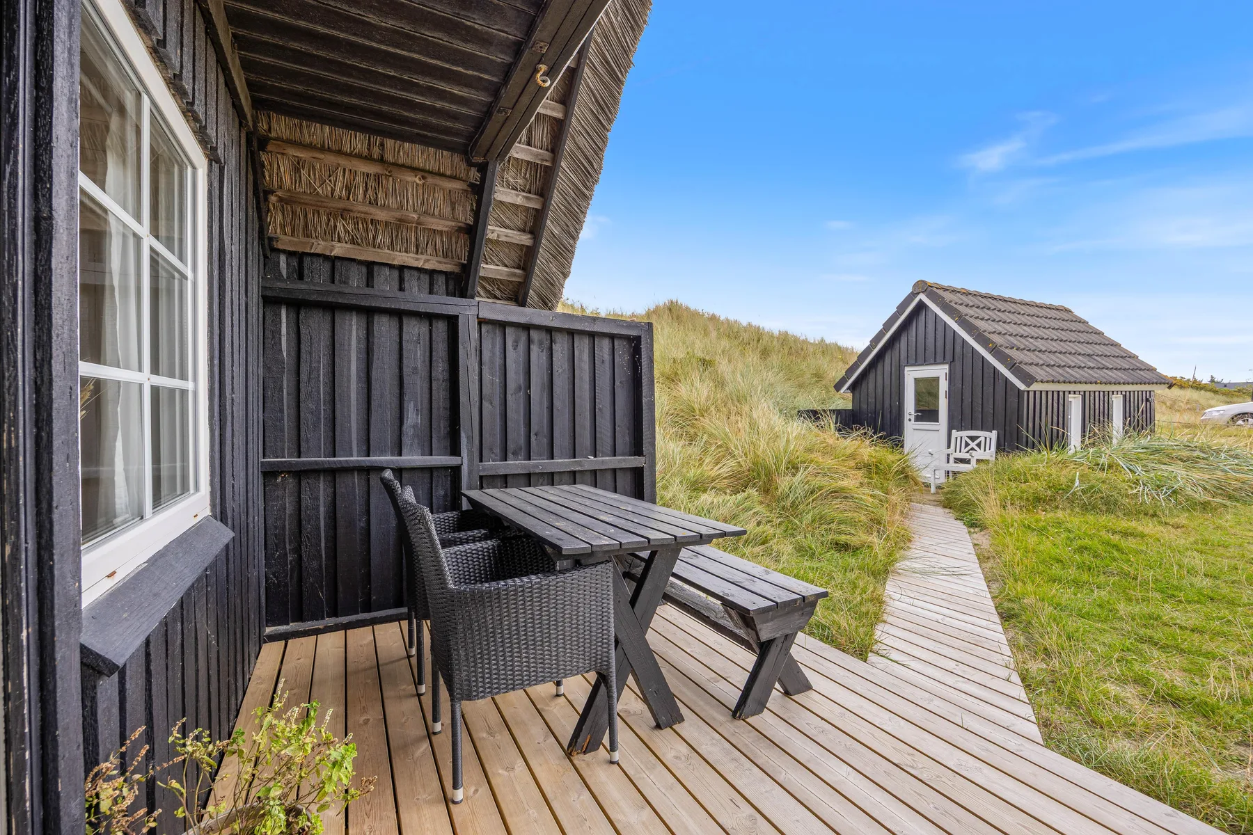 A wooden deck with outdoor seating overlooks a grassy path and small building.