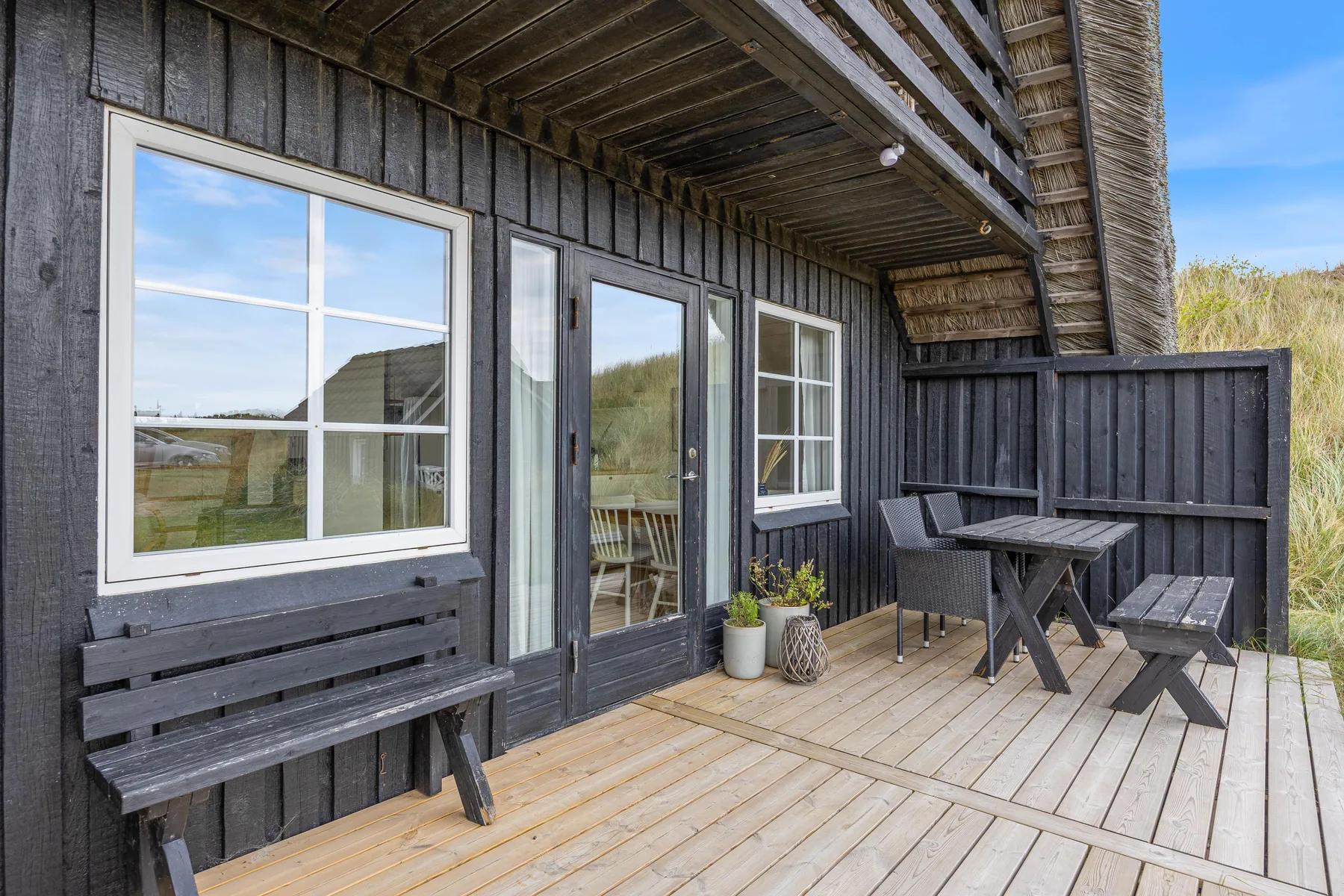 A wooden deck beside a dark-sided building has seating and a table.