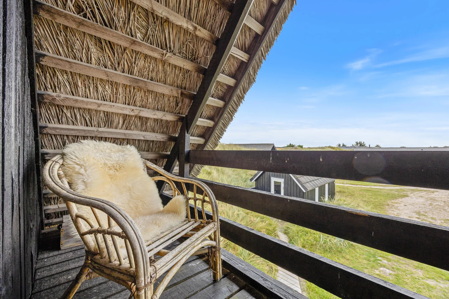 A covered balcony with a cushioned seating area overlooking open fields.