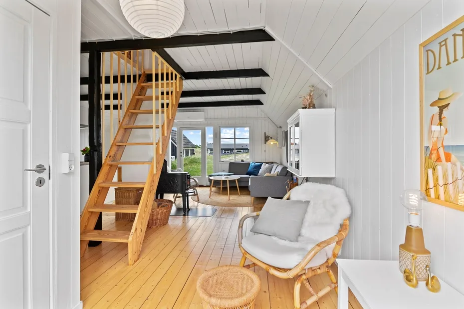 A bright living room with a wooden staircase and seating by the windows.