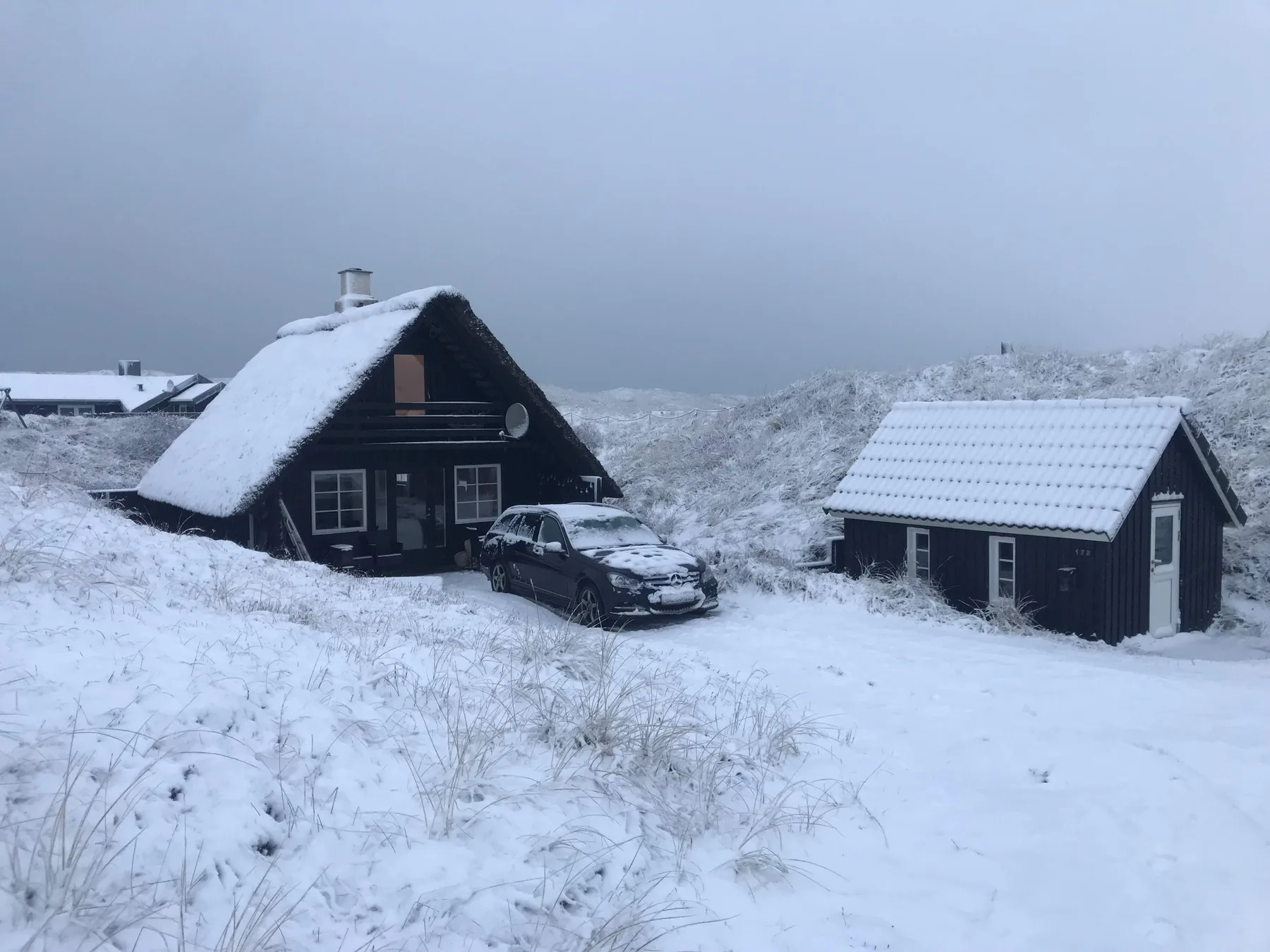 Snow-covered cabins stand beside a snowy path in a wintry landscape.