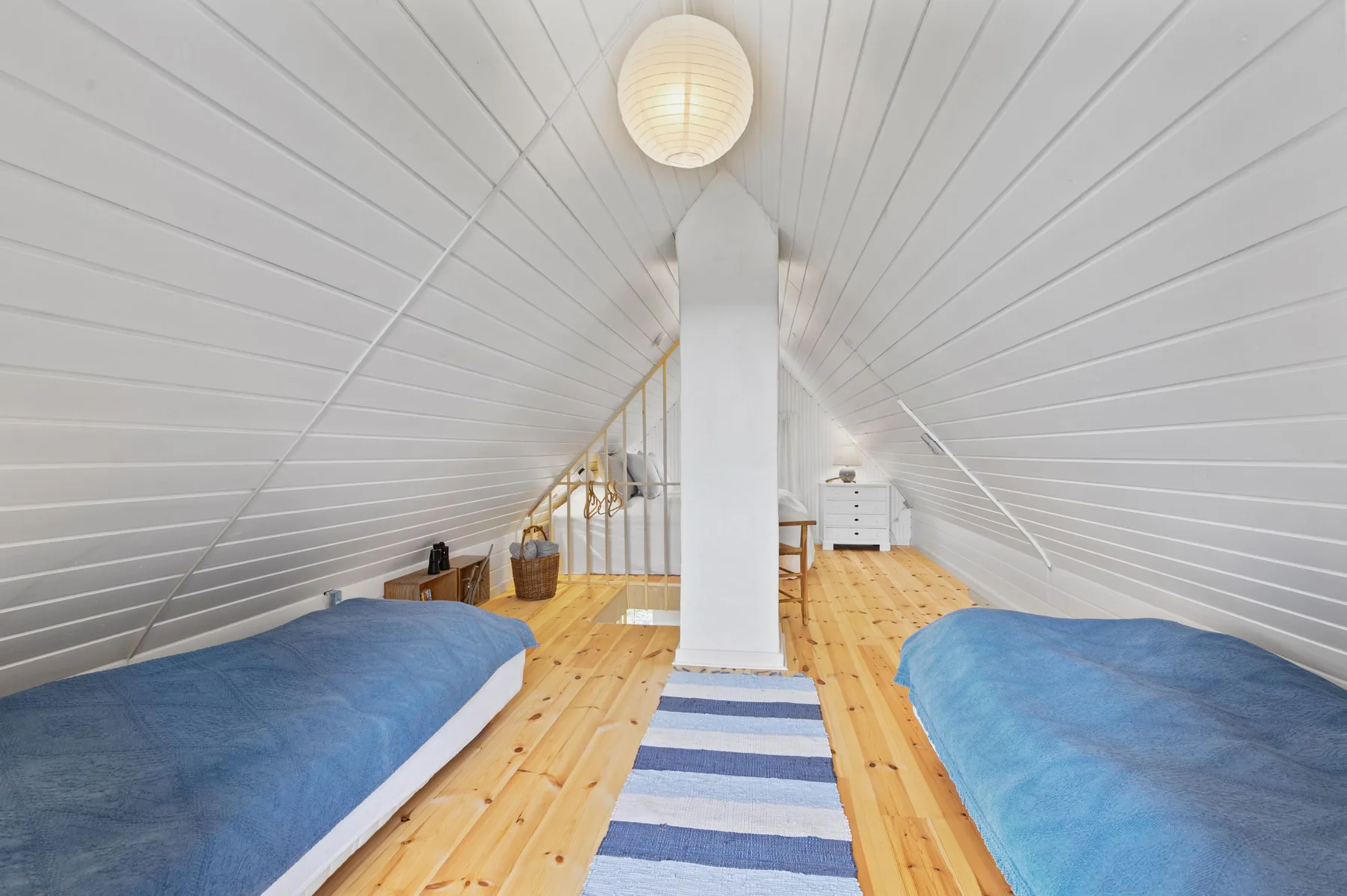 An attic bedroom with two beds beneath a sloped white ceiling.