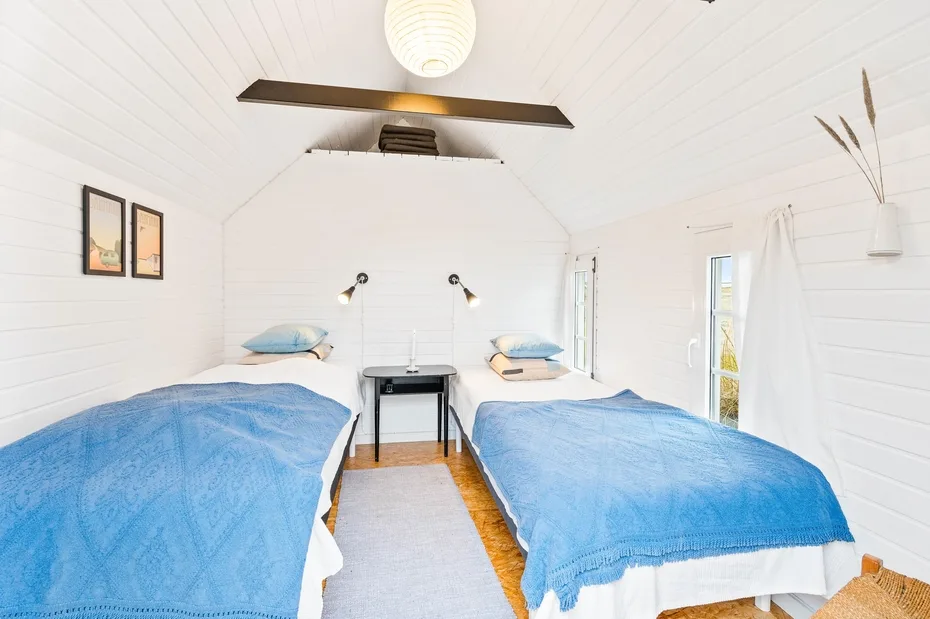 A bright bedroom with two beds covered in blue bedding.