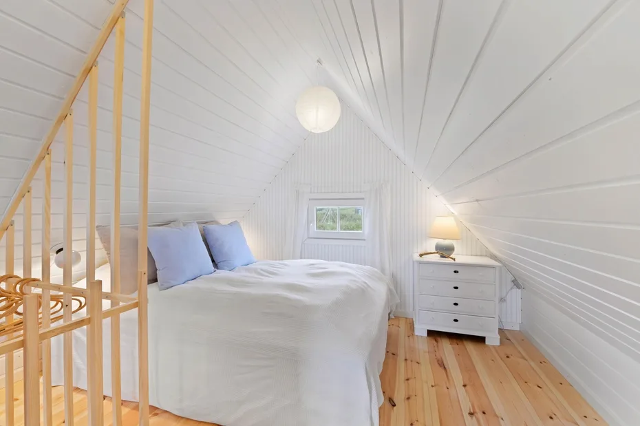 A bright attic bedroom with a bed, a small window, and a white dresser.