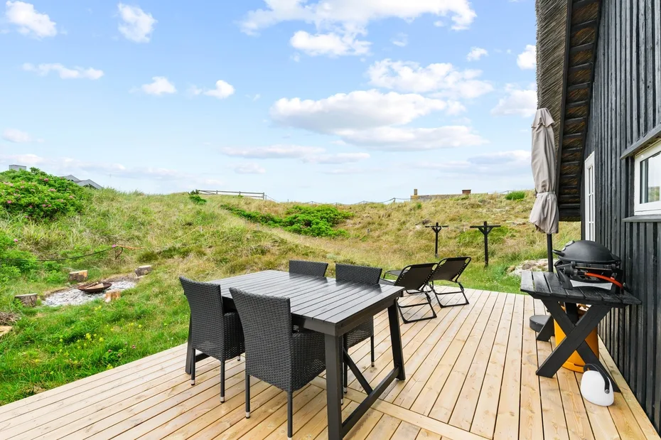 An outdoor deck with a dining table and seating overlooks a grassy landscape.