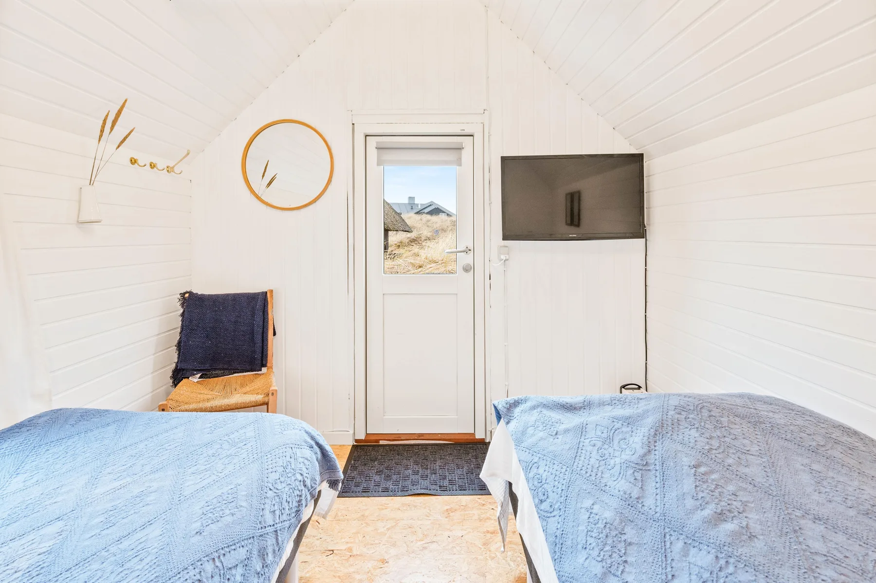 A bright bedroom with two beds and a door opening to an outdoor view.