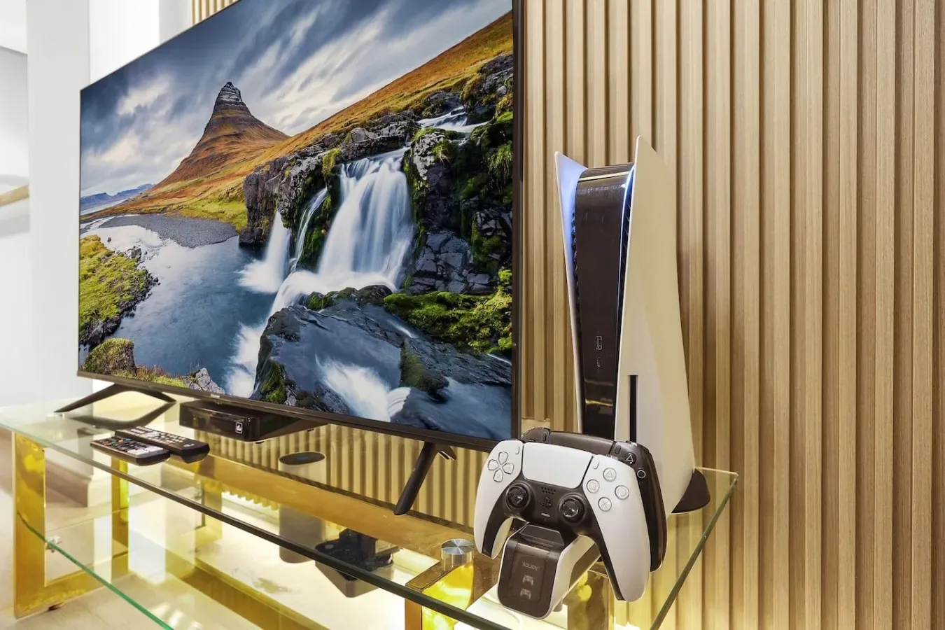 Un televisor muestra un paisaje con cascada junto a una consola y un mando.