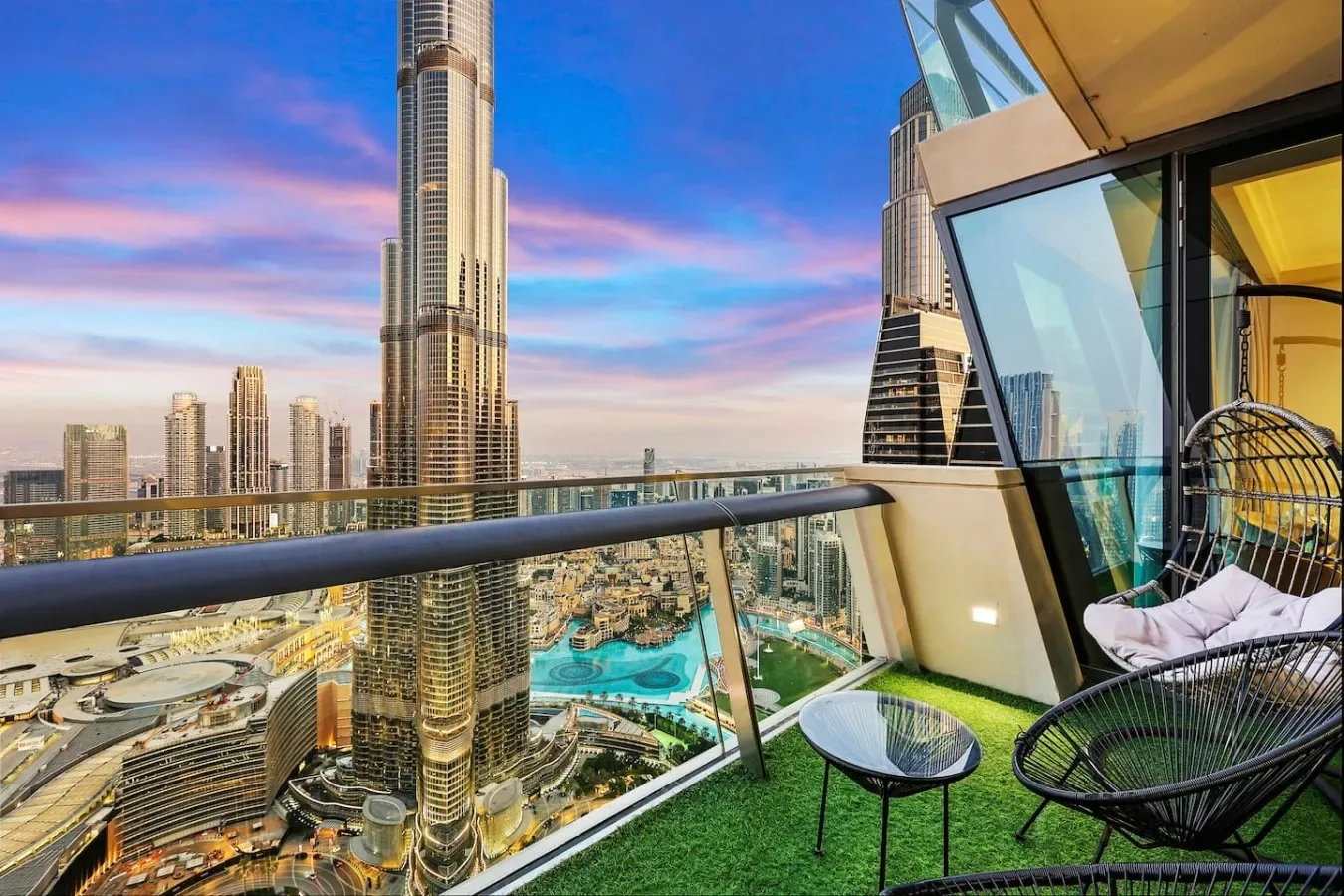A balcony with seating overlooks a city skyline and turquoise pool.