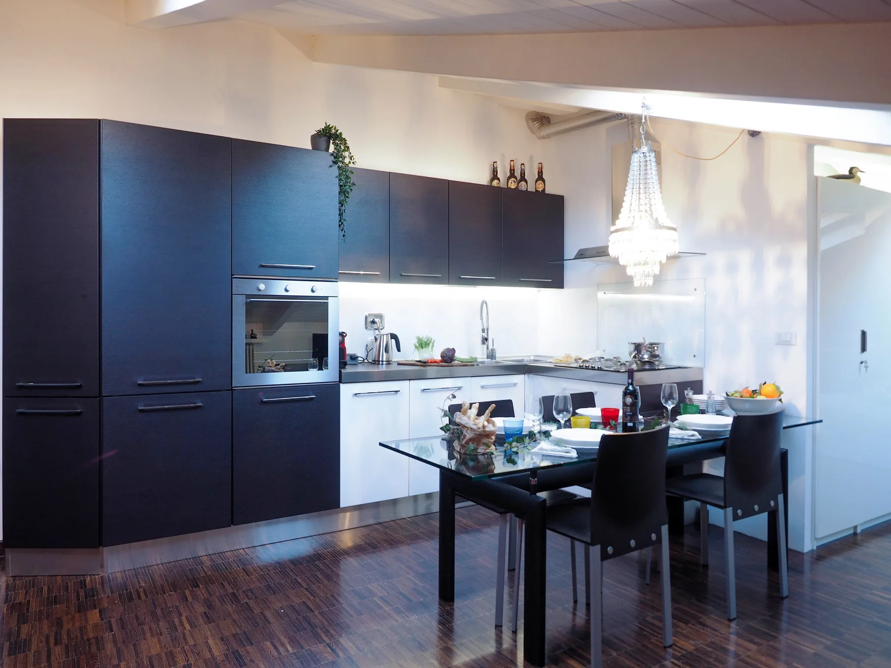 Una cocina moderna y zona de comedor con armarios oscuros y una mesa de vidrio.