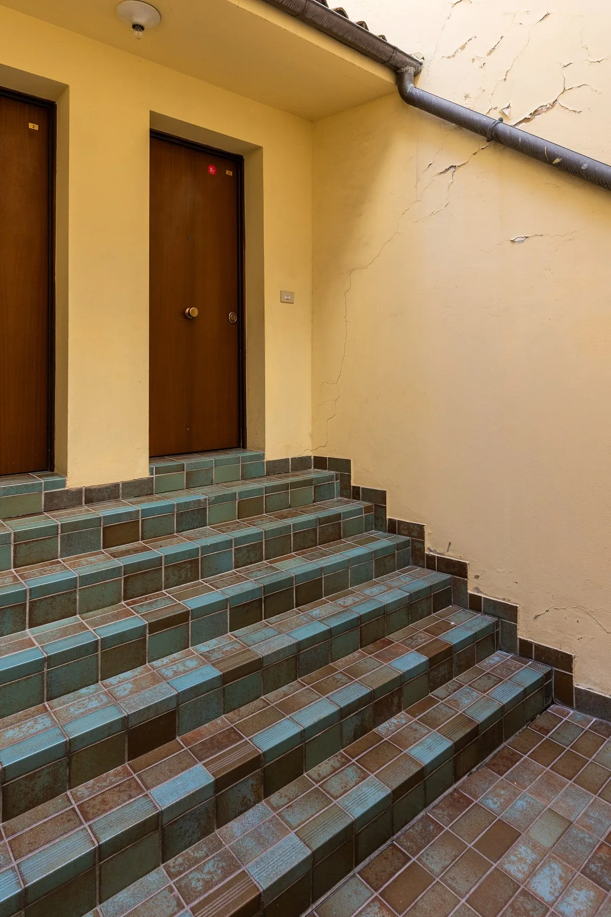 Escalones de azulejos conducen a puertas de madera en una entrada exterior amarilla.